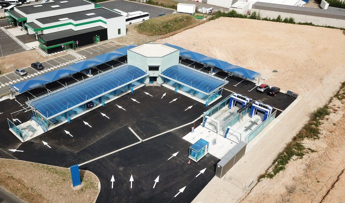 Vue aérienne d'une station de self-lavage : pistes couvertes, circulation fléchée et bâtiment technique